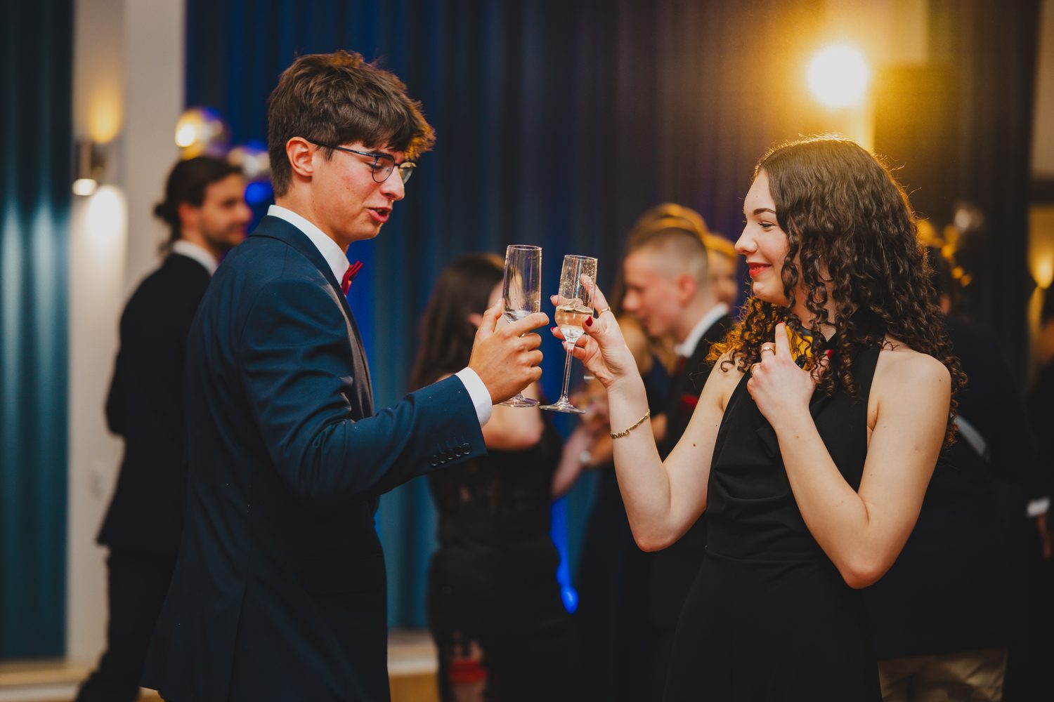 Para uczestników studniówki wznosi toast kieliszkami szampana